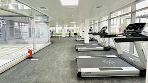 A gym with treadmills, a fire extinguisher, and large windows. - Bloomfields Studio Oasis Masdar (Abu Dhabi)