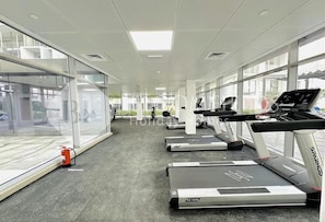 Ein Fitnessraum mit Laufbändern, einem Feuerlöscher und großen Fenstern.