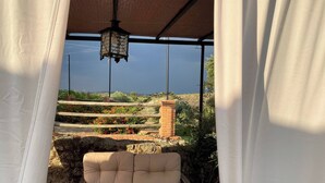 A covered outdoor seating area with a cushioned bench, a wooden table, and a view of a brick wall and greenery. - Detached 4 Bedroom Villa With Pool (Valencia de Alcantara)