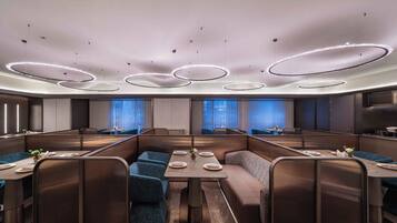 Un comedor moderno con asientos tipo cabina, luces de techo redondas y vistas de la ciudad a través de amplias ventanas.