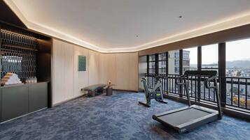 A hotel room with a large window, a treadmill, a bench, and a small exercise area.