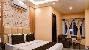 A modern hotel room with a large bed, a sofa, a desk, an air conditioning unit, and a ceiling fan. - Super Townhouse OAK Bulbuli Neer (Kalyani)