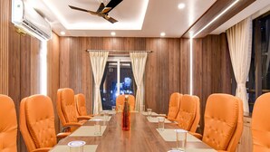 A conference room with a long table, orange chairs, and a ceiling fan. - Super Townhouse OAK Bulbuli Neer (Kalyani)