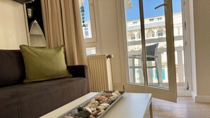 Ein Wohnzimmer mit einer Couch, einem Tisch mit einer Schale Steine, einem Fenster mit Blick auf Gebäude und einer Heizung.