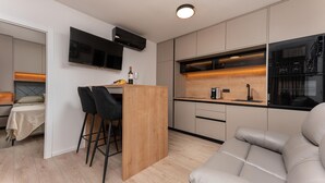 Ett kompakt kök med en bardisk i trä, en platt-TV och en modern kaffemaskin.