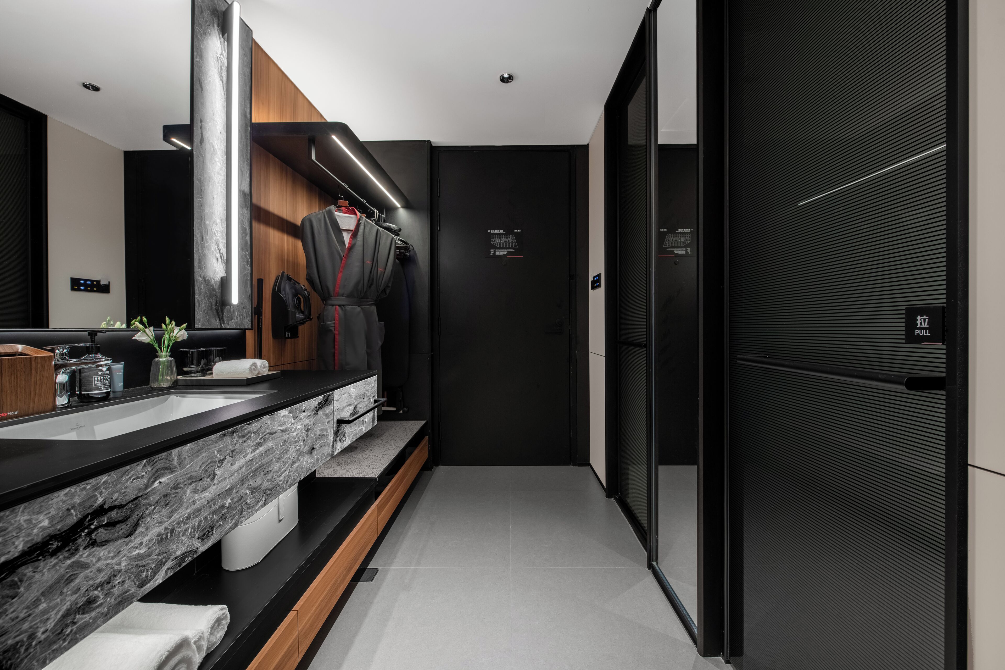 Une salle de bain moderne avec un comptoir en marbre, un porte-serviettes, un miroir et une porte noire dotée d’une poignée.