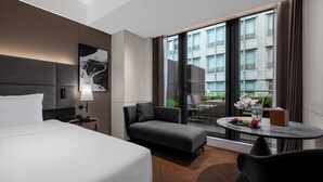A hotel room with a bed, a sofa, a small table with fruit, a lamp, and a view of the city through large windows. - IntercityHotel Shanghai World Expo Hotel (Shanghai)