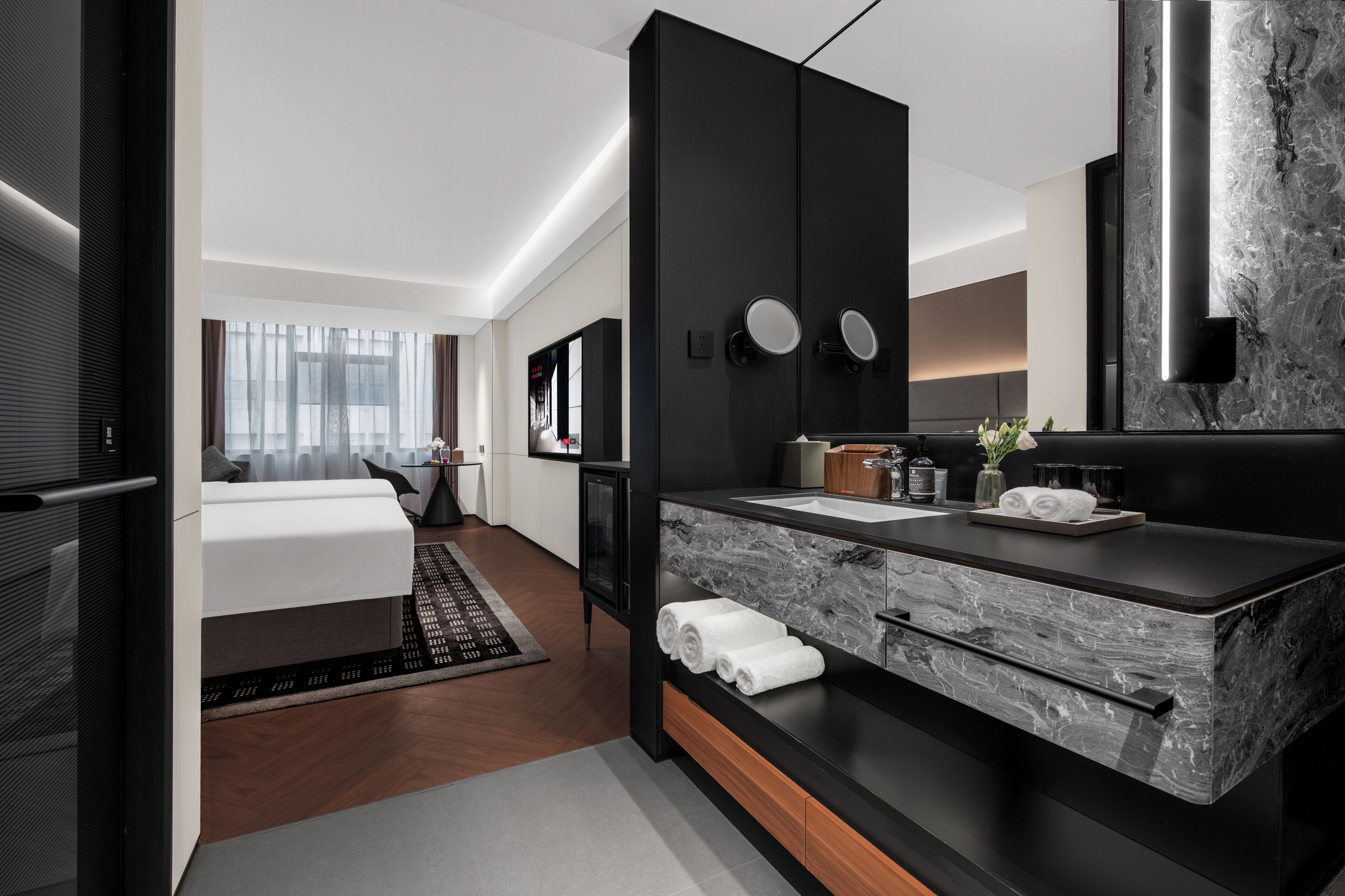 A modern hotel room with a large bed, a black vanity with a marble countertop, and a large mirror.