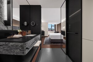 A modern hotel room with a marble sink, a bed, a large mirror, and a city view.