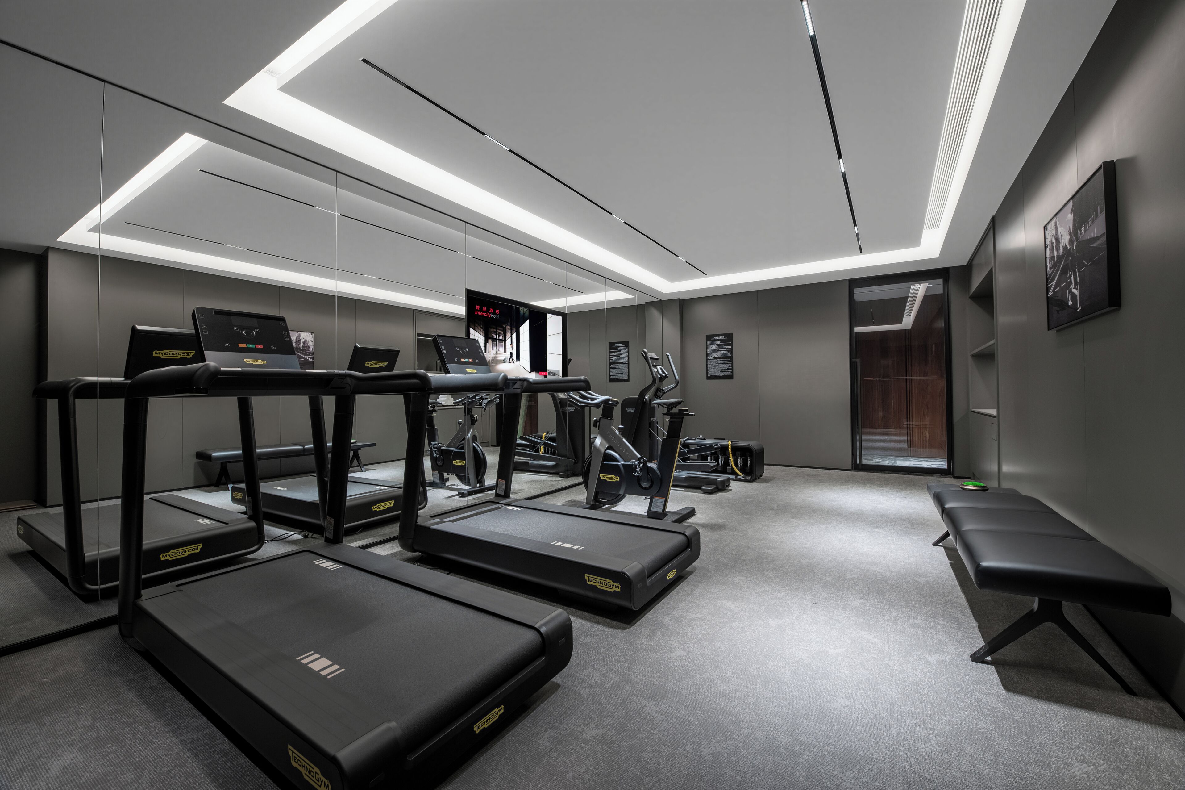 Une salle de sport moderne équipée de tapis de course, de vélos d’appartement et d’un banc de musculation.