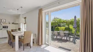 A dining area with a table and chairs, a kitchen in the background, and a sliding glass door leading to an outdoor patio. - Lavish 4-person beach villa in Makkum (Makkum)