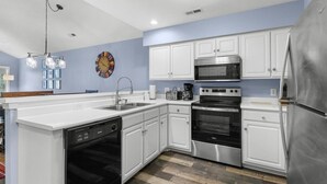 A modern kitchen with white cabinetry, stainless steel appliances, and a wooden floor. - True Blue Golf & Beach Getaway (Pawleys Island)