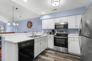 A modern kitchen with white cabinetry, stainless steel appliances, and a wooden floor. - True Blue Golf & Beach Getaway (Pawleys Island)