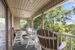 A covered porch with wooden chairs and tables, large windows, and a view of trees. - True Blue Golf & Beach Getaway (Pawleys Island)
