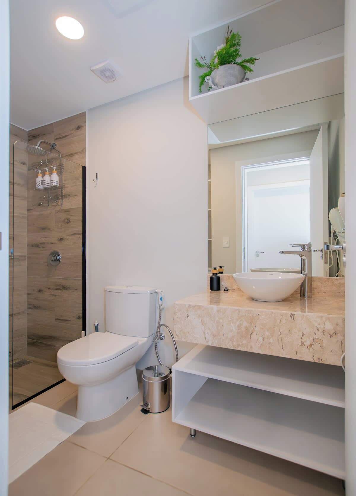 A modern bathroom with a glass-enclosed shower, a white toilet, a large sink, and a mirror above the vanity.