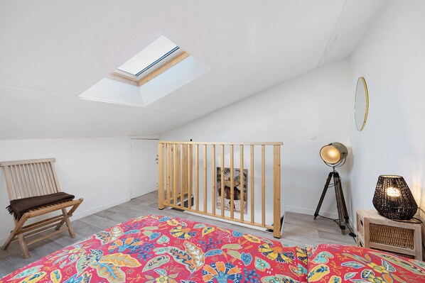 A room with a high ceiling, a skylight, a wooden crib, a floor lamp, and a patterned rug. - Charming Apartment for 4 with Shared Terrace and Garden (Saint-Jean-de-Liversay)