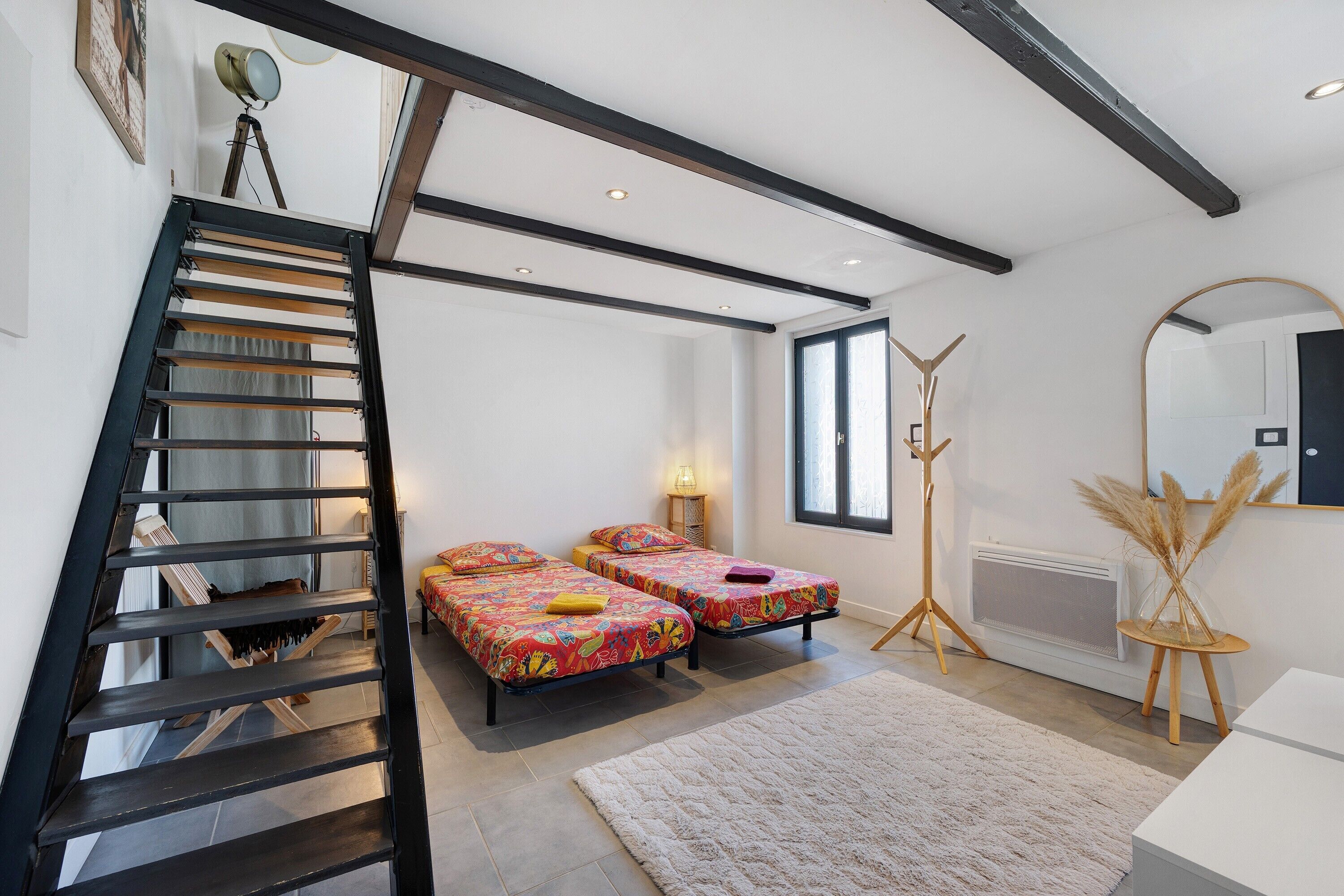 Une chambre avec deux lits, une échelle, un radiateur et une grande fenêtre.