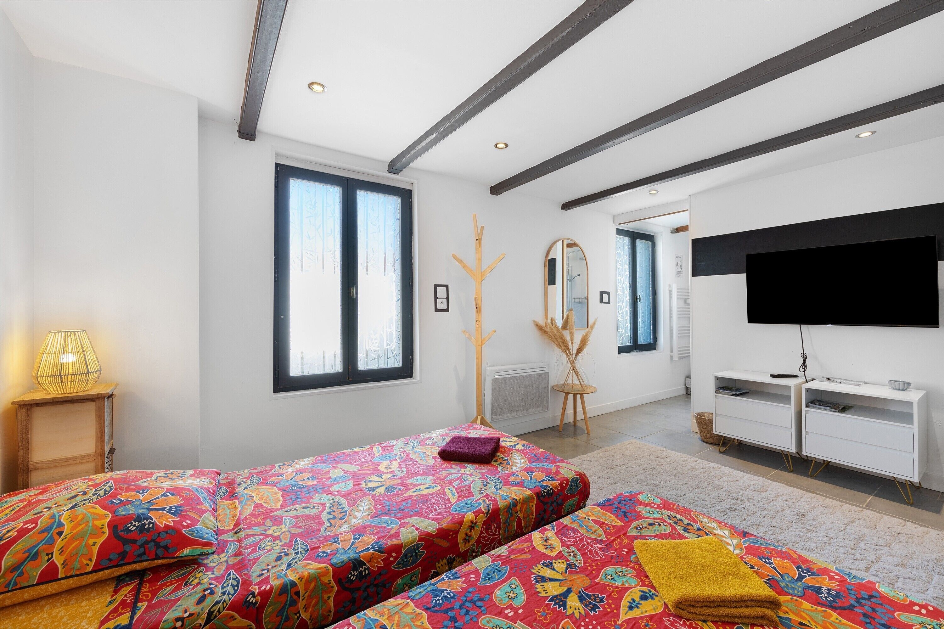 A modern bedroom with two beds, a TV, and a large window.