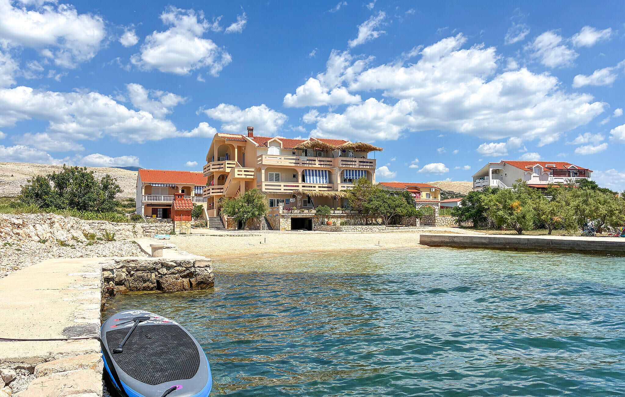 A coastal building with multiple balconies, a beach in the background, and clear skies.
