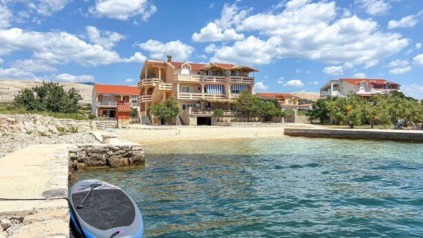 Um edifício costeiro com várias varandas, uma praia ao fundo e céu claro.