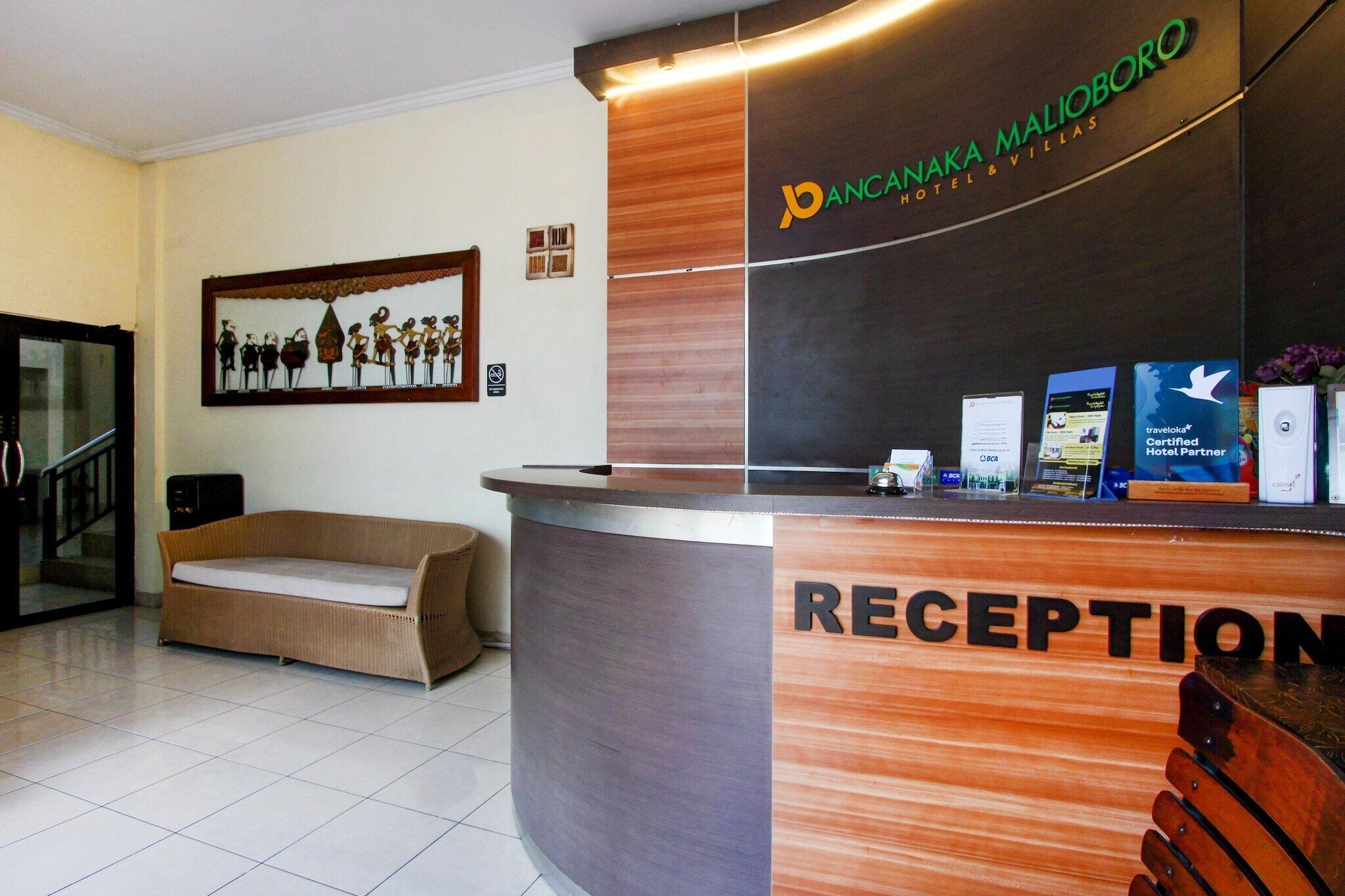 Una reception con il cartello 'Pananana Malioboro Hotel & Villas', un'opera d'arte incorniciata al muro e un divano sullo sfondo.