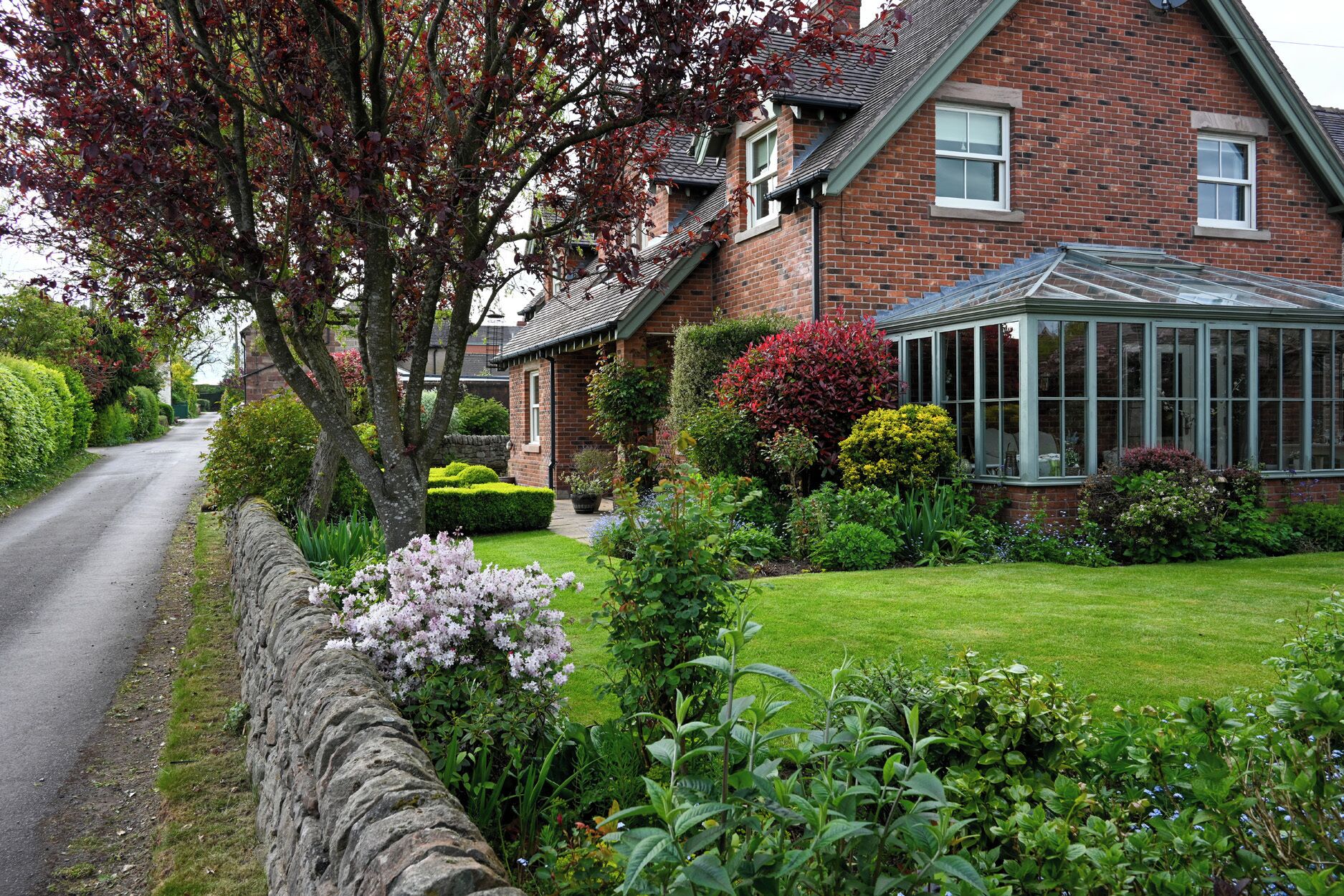 A brick house with a conservatory, a stone wall, and well-maintained gardens.