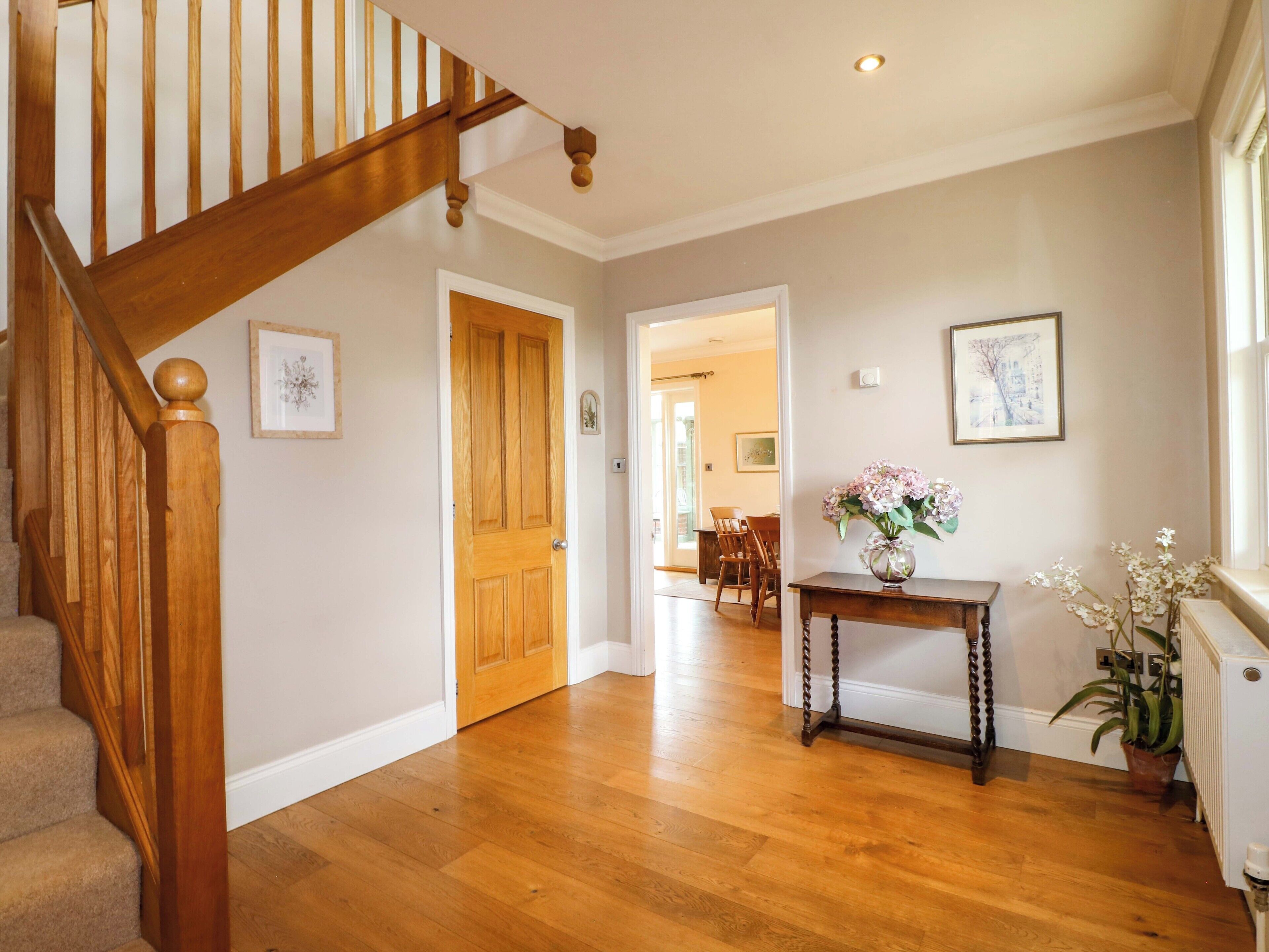A wooden staircase leading to a room with a wooden floor, a door, a table with a vase, and a potted plant.