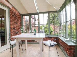 Un invernadero con pared de ladrillo, una mesa blanca, cuatro sillas y una botella de agua.