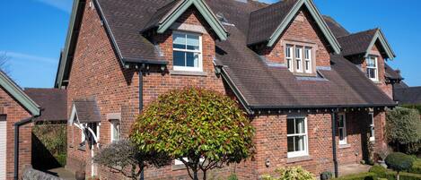A two-story brick house with a steeply pitched roof, a stone wall in front, and a well-maintained garden.