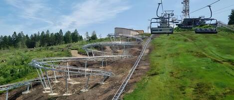 A ski lift system with tracks and cables, surrounded by greenery and a clear sky.
