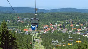 Un sistema de telefèric amb cabines numerades 30 i 67, una vila amb cases de teulades vermelles i un paisatge de bosc al fons.