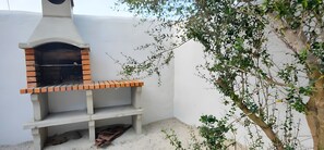 For forn de maó a l'aire lliure, amb xemeneia, una banca i un arbre de fullatge verd.