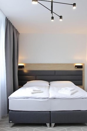 A modern hotel room with a bed, headboard, bedside lamps, and a window with curtains.