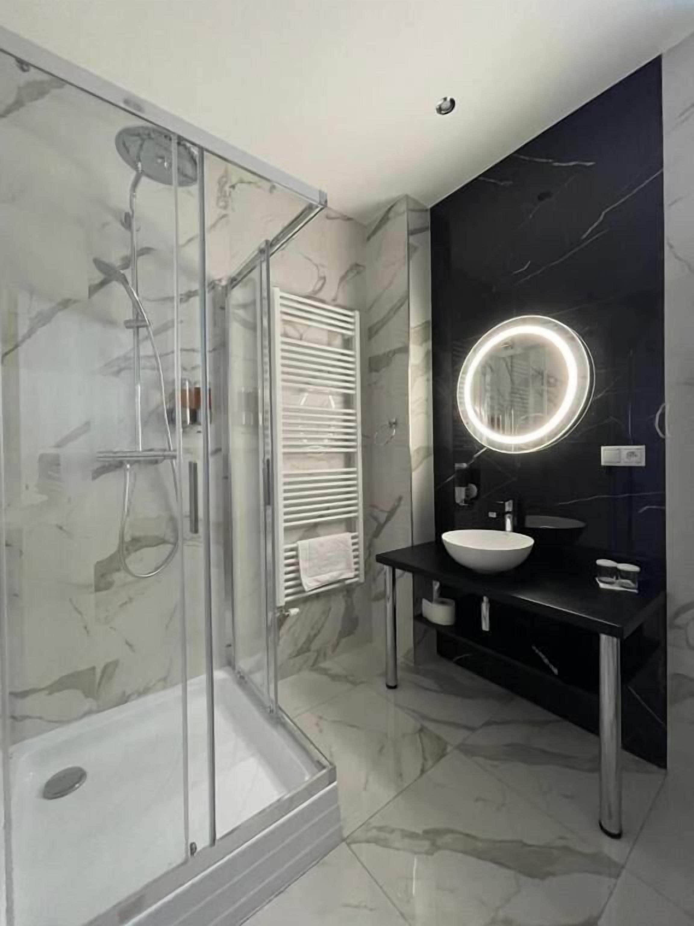 A modern bathroom with a glass-enclosed shower, a white sink, and a dark marble wall.