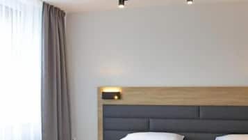 Habitación de hotel con dos camas, una lámpara moderna, un cabecero de madera y un amplio ventanal con cortinas.