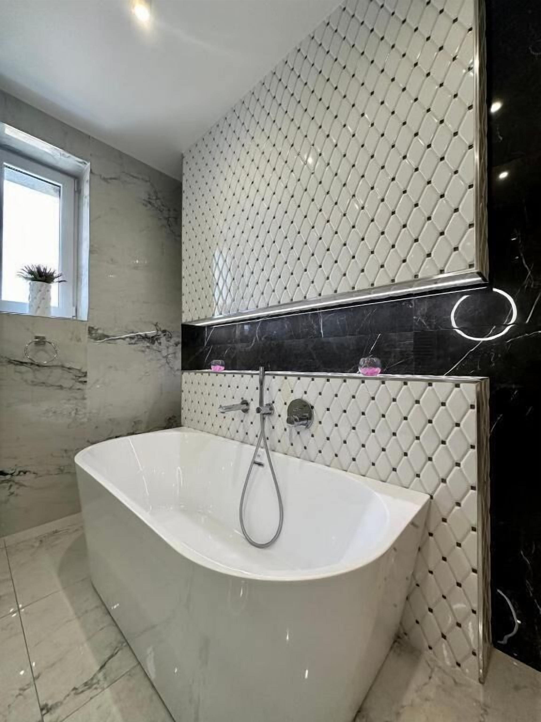 A modern bathroom with a freestanding bathtub, a marble floor, and a patterned wall.