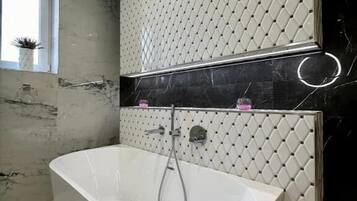 A modern bathroom with a freestanding bathtub, a marble floor, and a patterned wall.