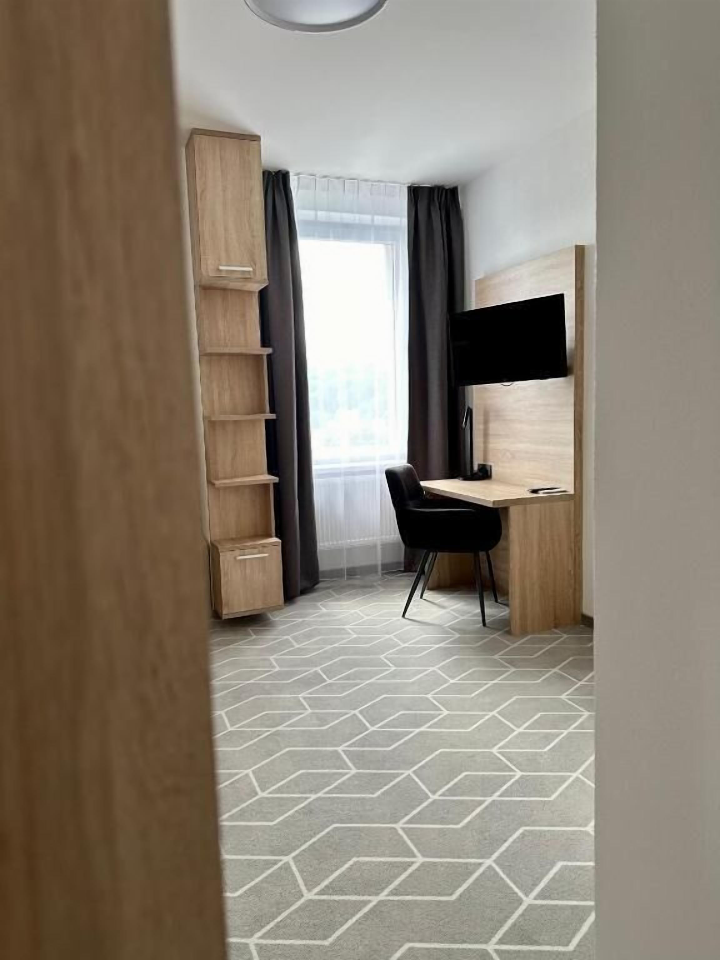 A room with a wooden desk, a chair, a TV, and a window with curtains.