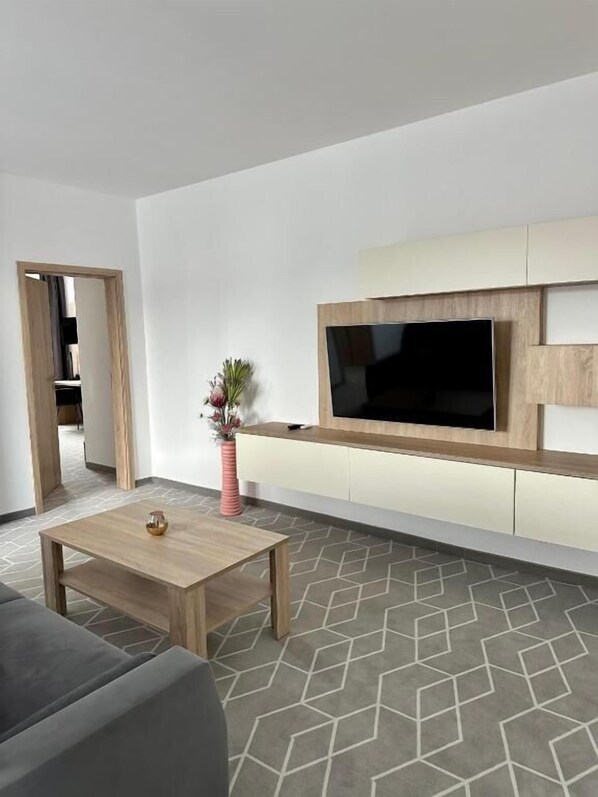 Una sala de estar moderna con un televisor de pantalla plana, una mesa de centro de madera y una alfombra estampada.