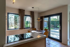A modern kitchen with a central island, large windows, and a dining area with chairs. - 4-Guest Bungalow near Texel Dunes (De Koog)