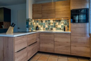 Eine moderne Küche mit Holzausstattung, Fliesenrückwand und eingebautem Ofen.