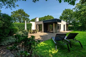 Una casa moderna con un patio, mobiliario exterior y un jardín bien cuidado.