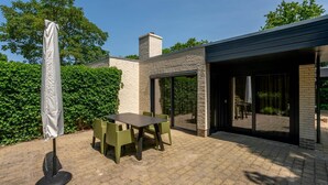 Un patio con mesa y sillas, una sombrilla y un edificio moderno con ventanas amplias y fachada de ladrillo.