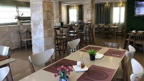 Comedor de hotel con pilares de piedra, varias mesas, sillas y una pared verde con un televisor.