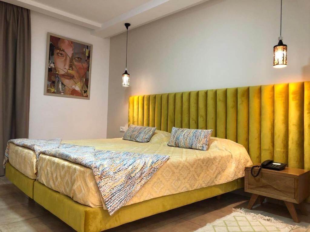 Un lit avec une tête de lit jaune, une table de chevet avec une lampe et un tableau accroché au mur.