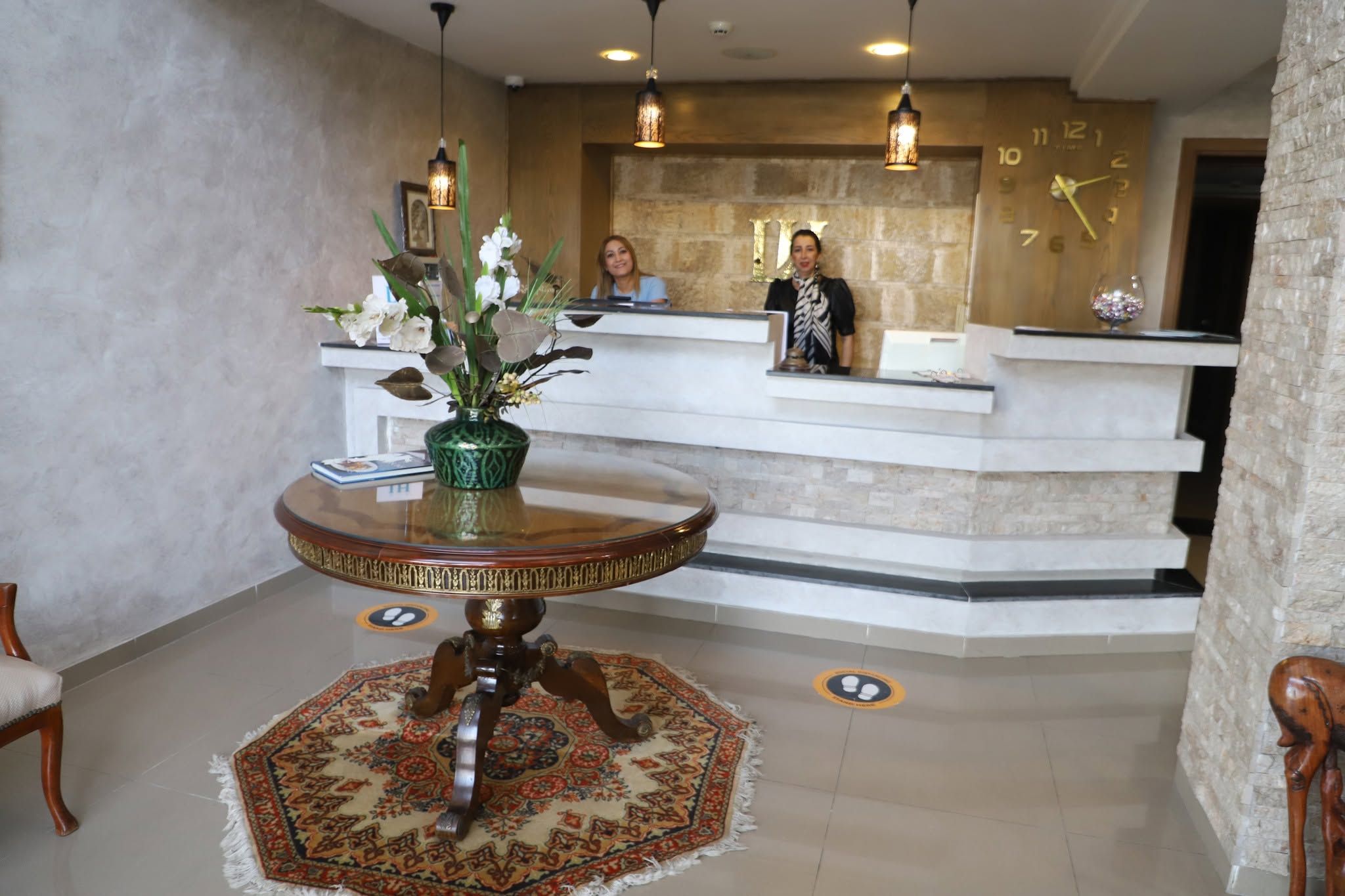A reception area with a round wooden table, a green vase with flowers, and a patterned rug.