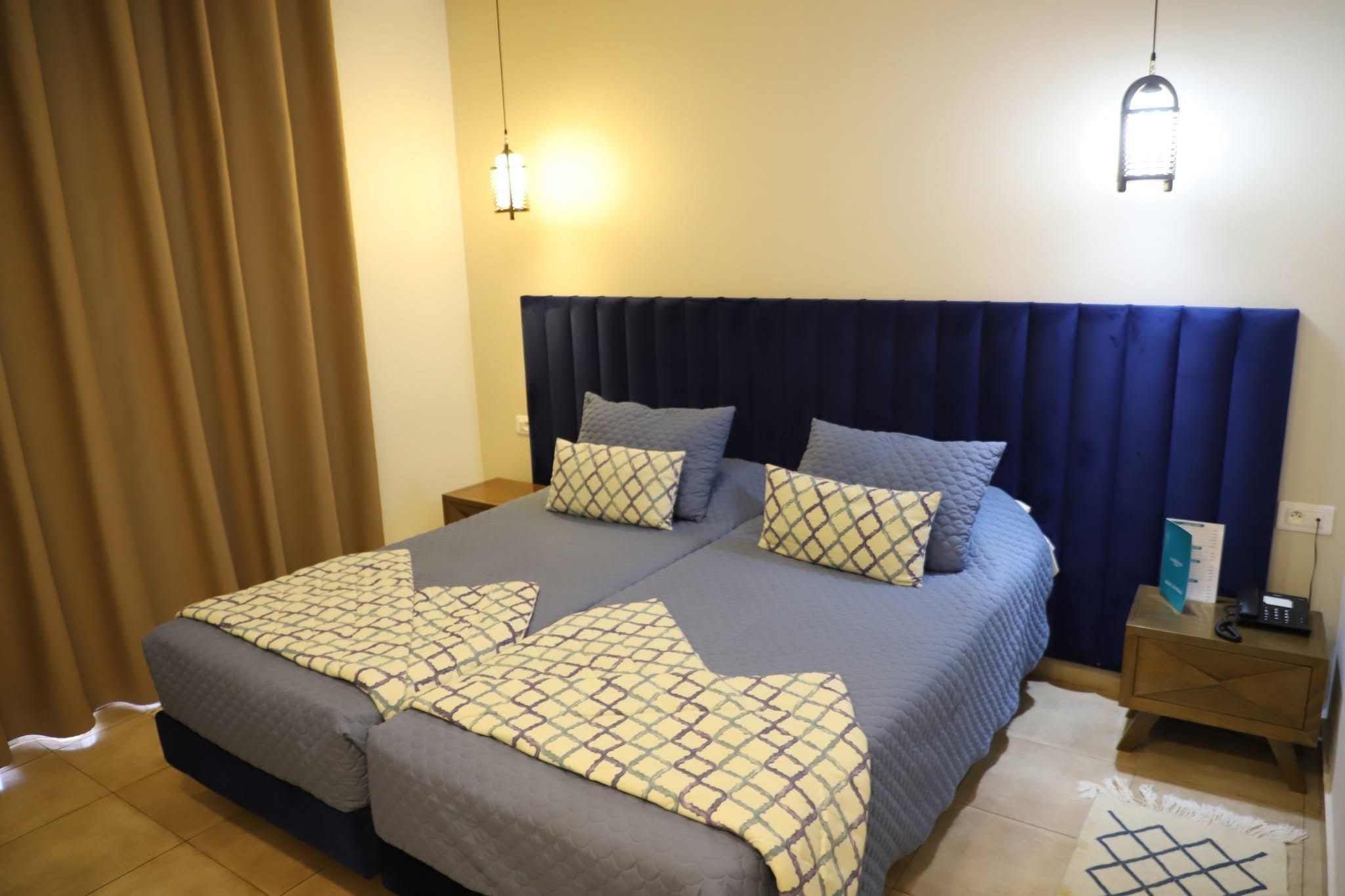Cama doble con ropa de cama estampada, dos mesitas de noche y una lámpara de pared.