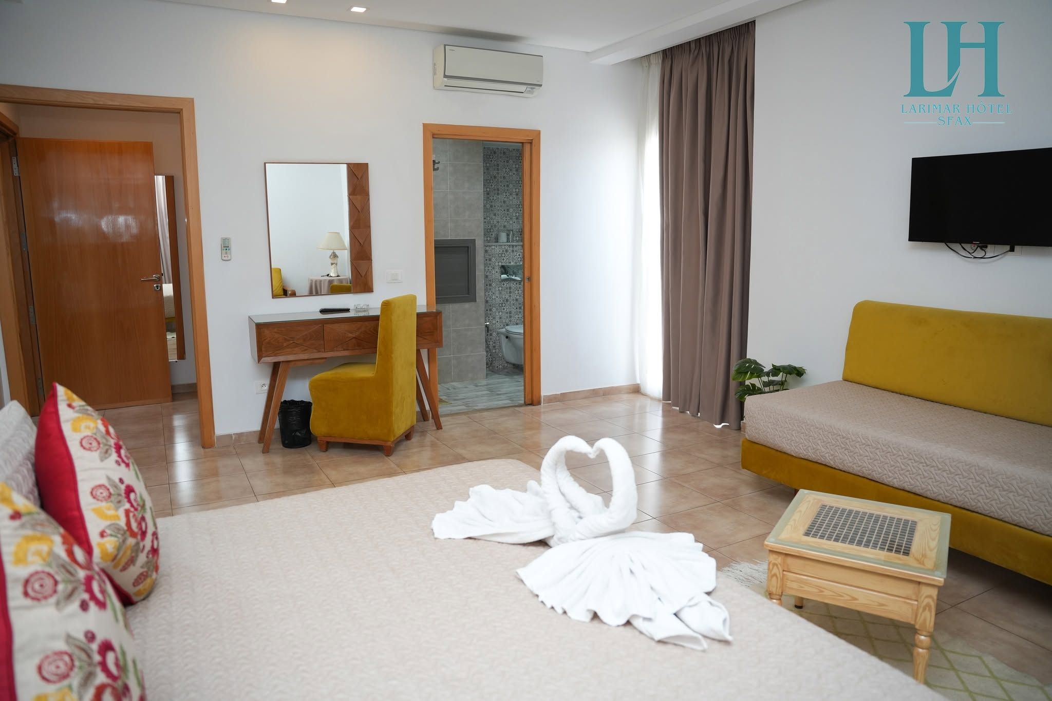 Habitación de hotel con sofá, escritorio con silla, televisor y una decoración de toallas con forma de cisne.