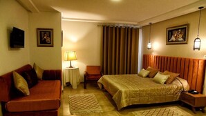 Una habitación de hotel con una cama, un sofá, una mesita, una lámpara y cortinas.