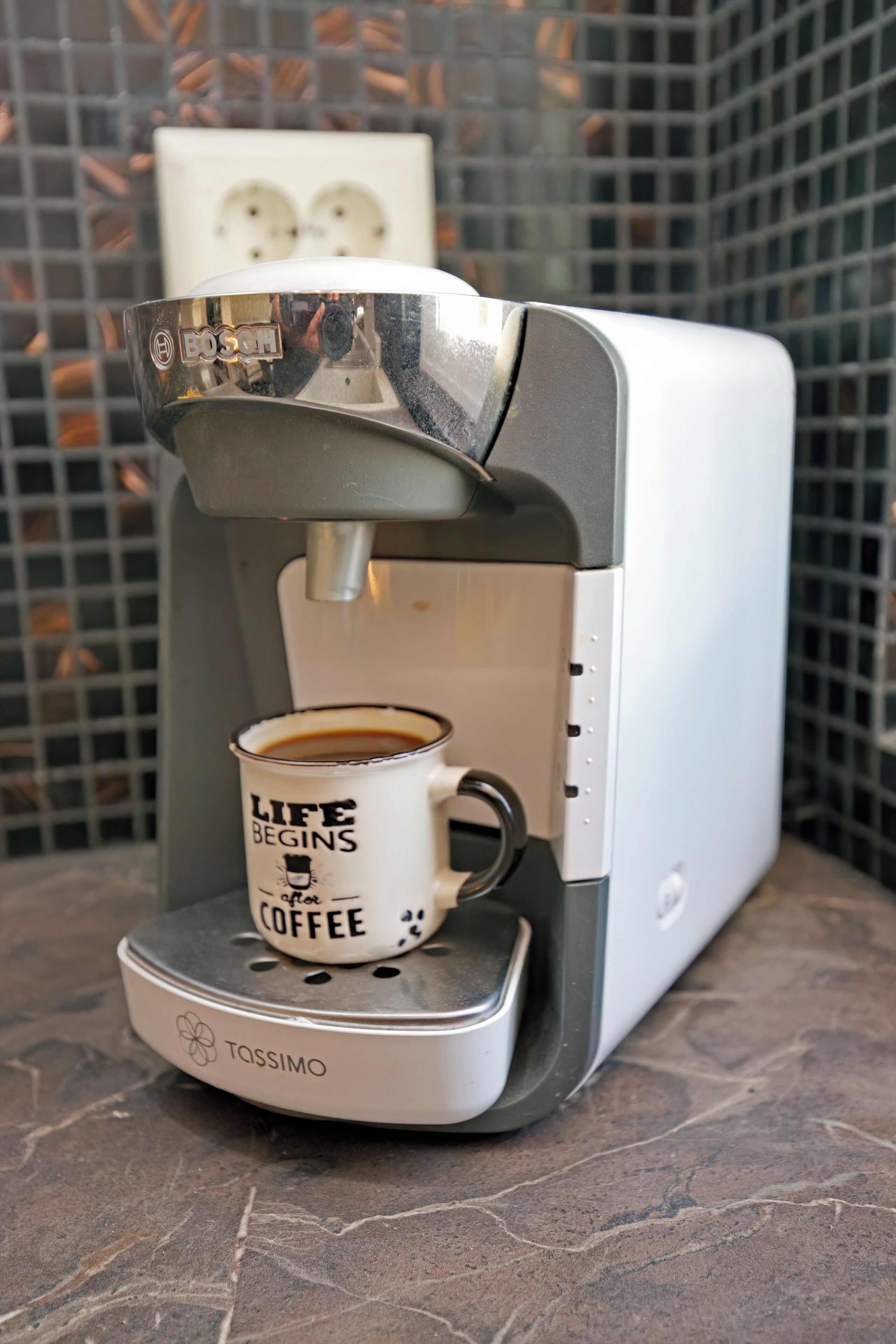 A Tassimo coffee machine dispensing coffee into a mug with 'Life Begins Coffee' text.